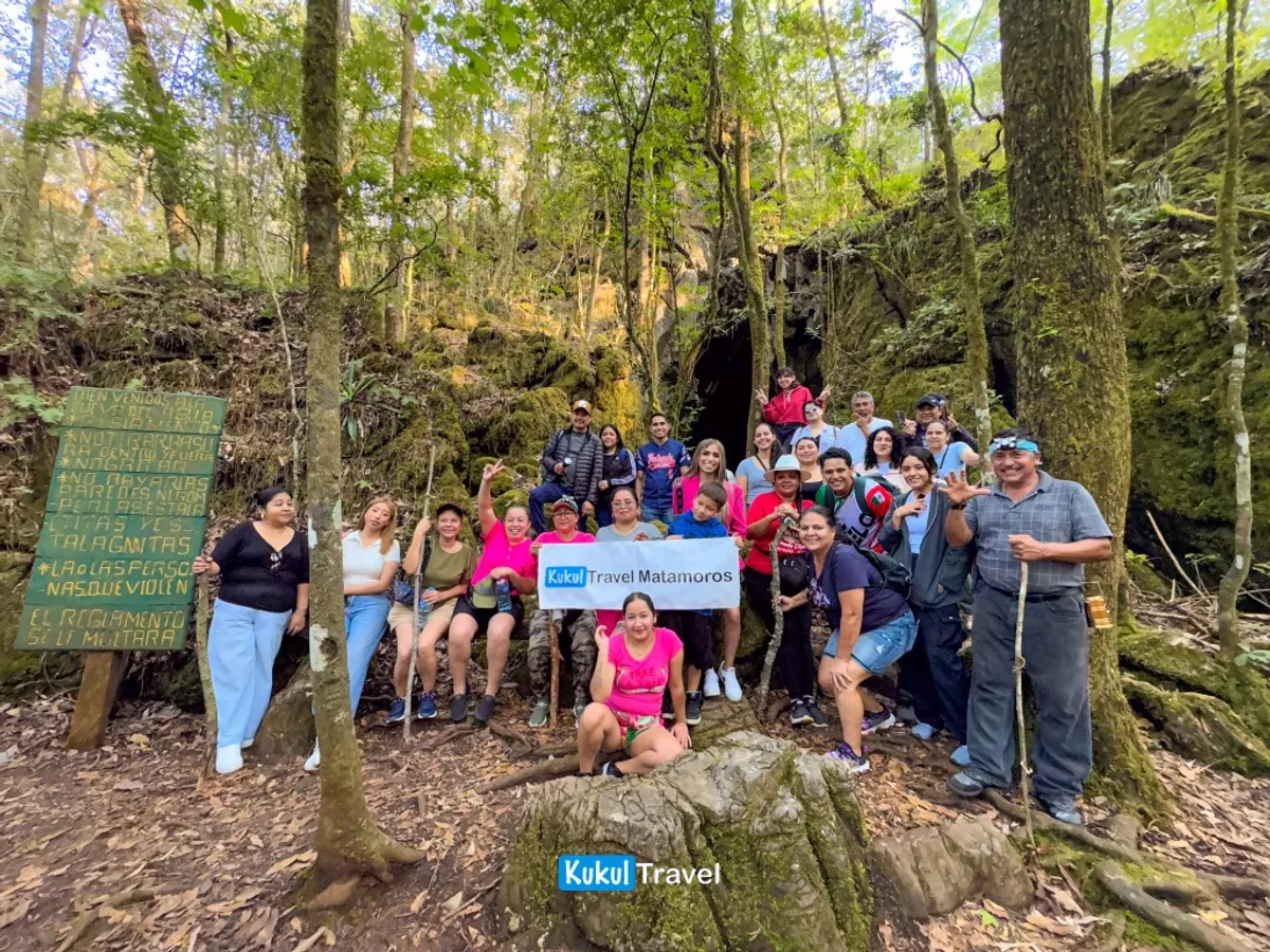 Grupo de visitantes en la entrada de Cueva del Agua con letrero de bienvenida y bosque de la Reserva de la Biosfera "El Cielo"