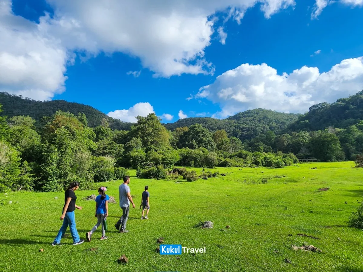 Familia caminando por el prado verde del Valle de Viveros con montañas boscosas al fondo, rama desde San José en la Reserva de la Biosfera "El Cielo"